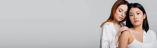 Brünette asiatin und rotschopf modell posiert isoliert auf grau, banner — Stockfoto