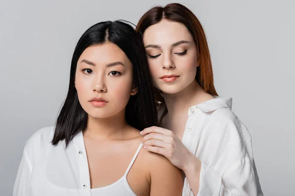 Redhead model posing with brunette asian woman isolated on grey — Stock Photo