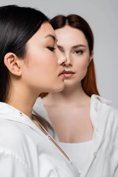 Perfil de modelo asiático posando cerca borrosa pelirroja aislada en gris - foto de stock