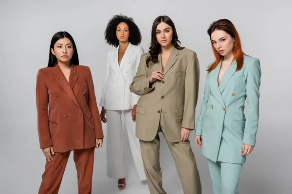 Grupo multiétnico de modelos en trajes de color pastel posando en gris — Stock Photo