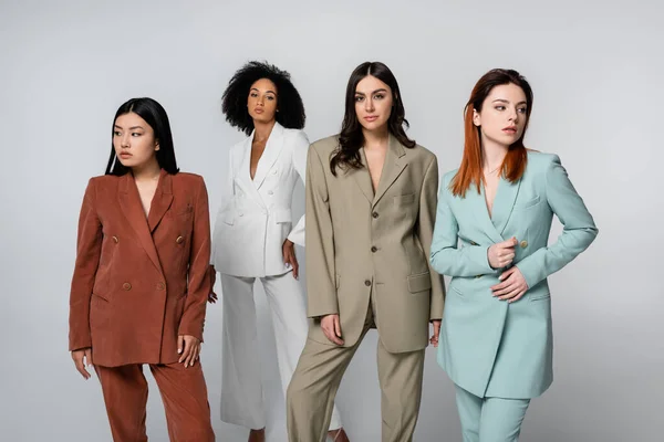 Modelos jóvenes interracial en trajes de color pastel posando en gris - foto de stock