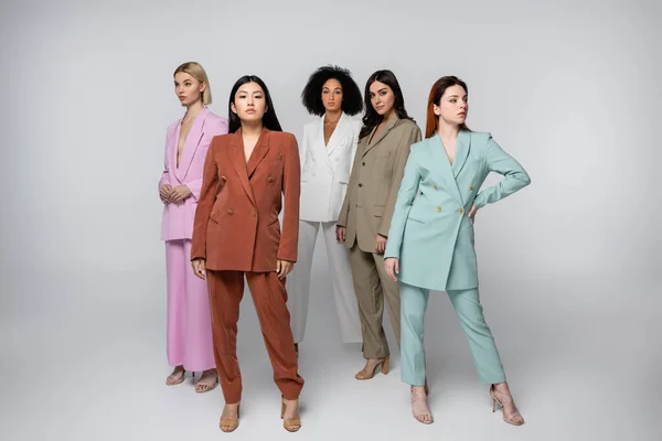 Full length of interracial models in stylish pastel suits posing on grey — Stock Photo