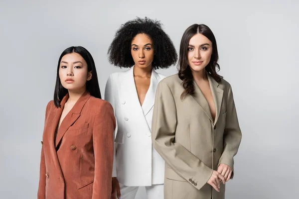 Young interracial women in trendy suits posing isolated on grey — Stock Photo