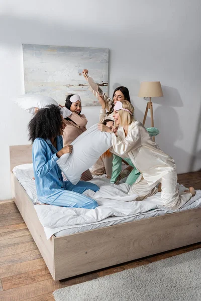 Groupe de joyeux amis interracial en pyjama ayant bataille d'oreillers pendant la soirée pyjama — Photo de stock