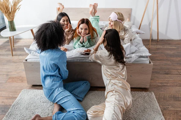 Grupo de mujeres sonrientes multiétnicas hablando durante la fiesta de pijamas - foto de stock