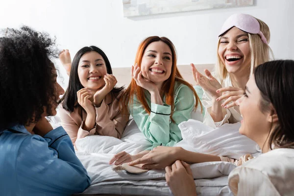 Grupo de mujeres multiétnicas felices hablando y riendo durante la fiesta de pijamas - foto de stock