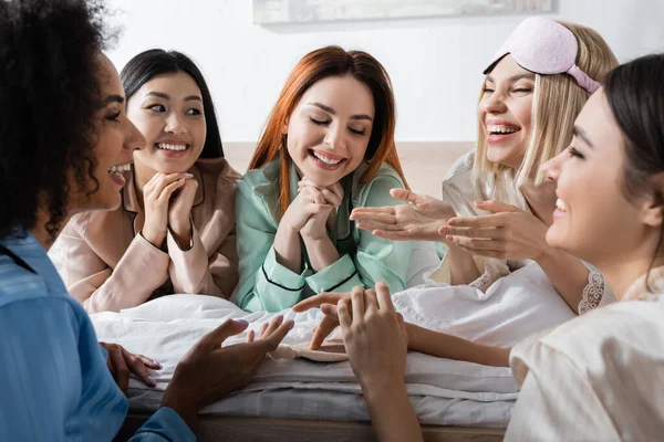 Grupo de mulheres multiétnicas alegres conversando e rindo durante a festa do pijama — Fotografia de Stock