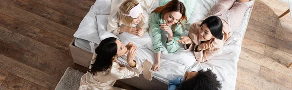 Vista ad alto angolo del gruppo di donne interrazziale compiaciute che parlano durante il pigiama party, banner — Foto stock