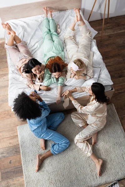 High angle view of happy interracial women lying on bed during slumber party — Stock Photo