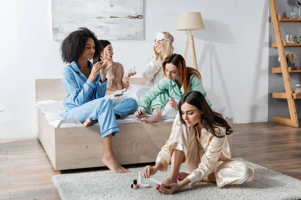 Alegre interracial las mujeres haciendo belleza procedimientos durante slumber fiesta - foto de stock