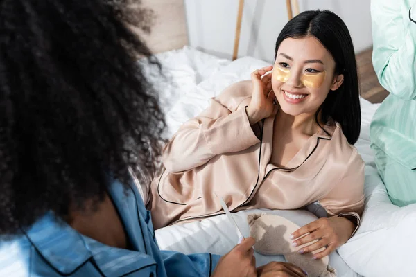 Gai asiatique femme avec oeil patches sourire tout en regardant flou afro-américain ami pendant somnambule partie — Photo de stock