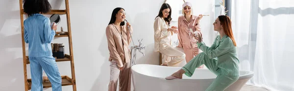 Happy interracial women in eye patches smiling in bathroom during slumber party, banner — Stock Photo