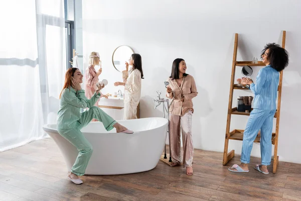 Счастливые межрасовые женщины в глазных повязках улыбаются в ванной во время пижамной вечеринки — стоковое фото