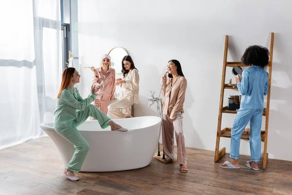 Cheerful interracial women in eye patches smiling in bathroom during slumber party — Stock Photo