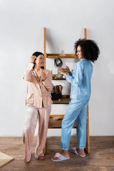 Heureux asiatique femme dans les yeux patches tenant sérum et en regardant afro-américain ami — Photo de stock