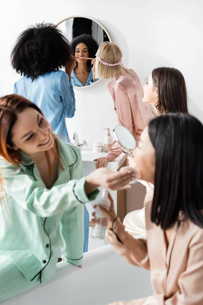 African american woman brushing teeth near blurred friends in bathroom — Stock Photo