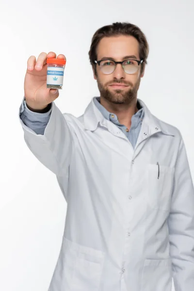 Médico borroso sosteniendo cannabis medicinal seco en un recipiente aislado en blanco - foto de stock