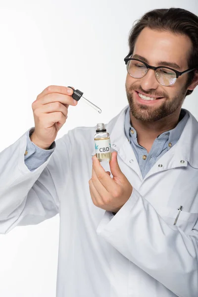 Medico sorridente che tiene flaconcino e contagocce di olio cbd isolato su bianco — Foto stock