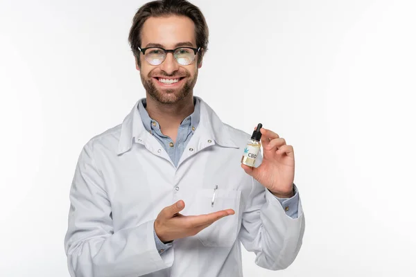 Médico feliz señalando vial con aceite de cáñamo aislado en blanco — Stock Photo