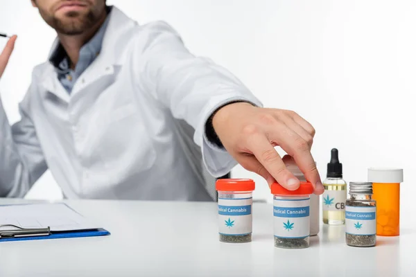 Cropped view of blurred doctor taking container with dry medical cannabis isolated on white — Stock Photo