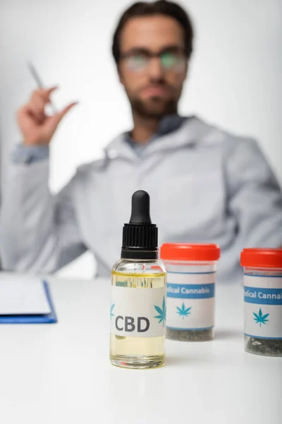 Foyer sélectif de l'huile de cbd et du cannabis médical sec près du médecin flou isolé sur blanc — Photo de stock