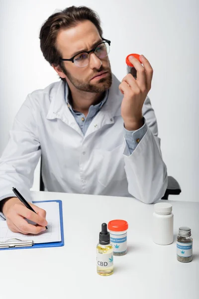 Arzt betrachtet medizinische Hanfmedikamente, während er Rezepte isoliert auf weißem Papier schreibt — Stockfoto