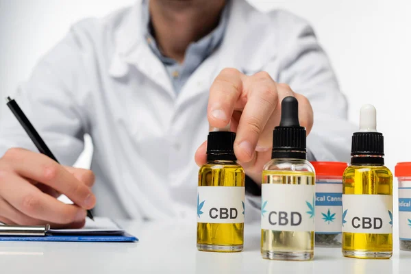 Abgeschnittene Ansicht von verschwommenen Arzt Schreiben Rezept in der Nähe von Fläschchen mit cbd-Öl isoliert auf weiß — Stockfoto