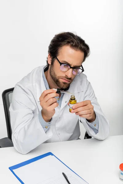 Лікар тримає флакон і крапельницю з олією КДБ біля буфера обміну інформацією ізольовано на білому — стокове фото
