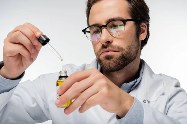 Medico in occhiali che tiene contagocce e bottiglia di olio cbd isolato su bianco — Foto stock