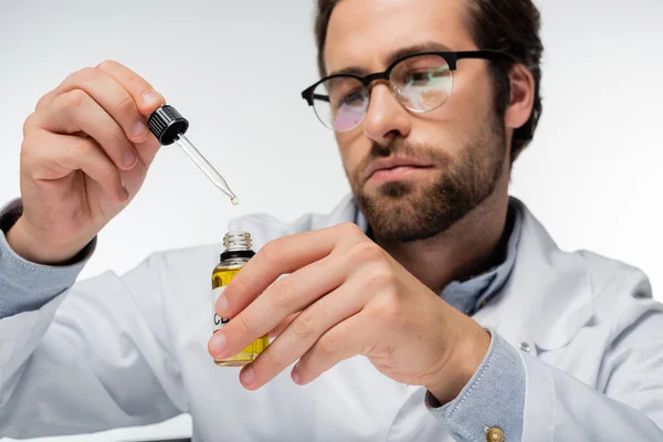 Doctor borroso sosteniendo botella y gotero con aceite de cannabis aislado en blanco - foto de stock