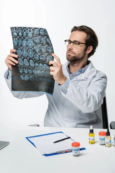 Médecin dans les lunettes de vue en regardant mri scan près de prescription et des conteneurs avec du cannabis médical isolé sur blanc — Photo de stock