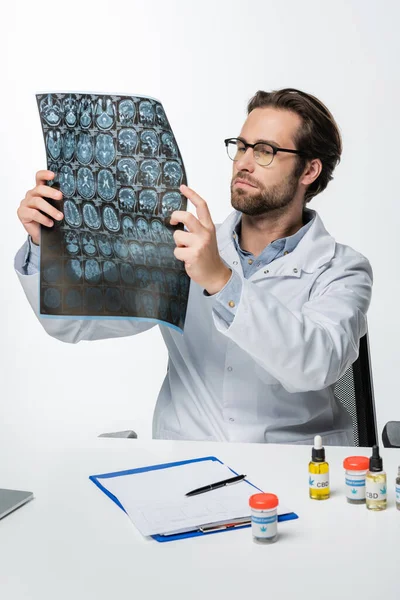 Doctor in eyeglasses looking at mri scan near prescription and containers with medical cannabis isolated on white — Stock Photo