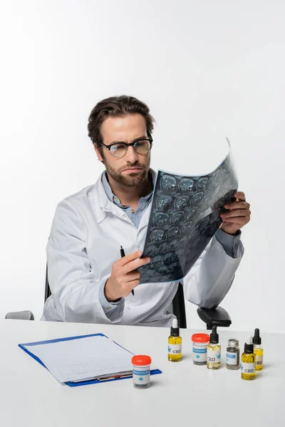 Physician looking at mri scan near clipboard and medical cannabis medication isolated on white — Stock Photo