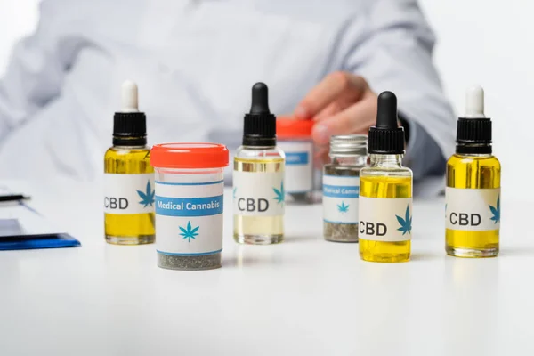 Vista recortada de un médico borroso cerca de contenedores y viales con medicamentos de cannabis medicinal aislados en blanco - foto de stock