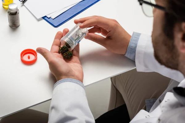Abgeschnittene Ansicht eines verschwommenen Arztes, der trockenes medizinisches Hanf in der Nähe des weißen Schreibtisches hält — Stock Photo