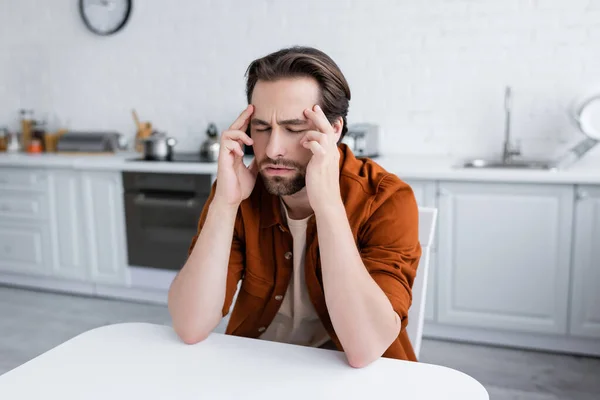 Mann berührt Kopf, während er unter Kopfschmerzen in Küche leidet — Stockfoto