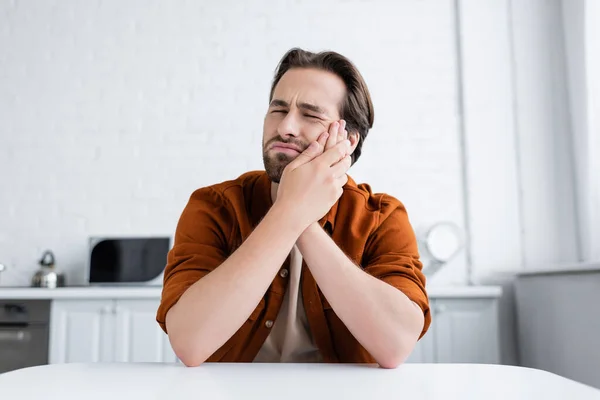 Frowning man touching cheek while suffering from toothache in kitchen — Stock Photo