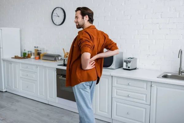 Hombre tocando la espalda mientras sufre de dolor en la cocina - foto de stock