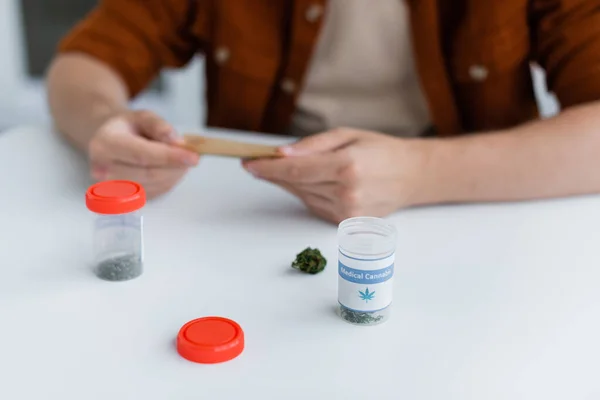 Cropped view of blurred man making joint with medical cannabis — Stock Photo