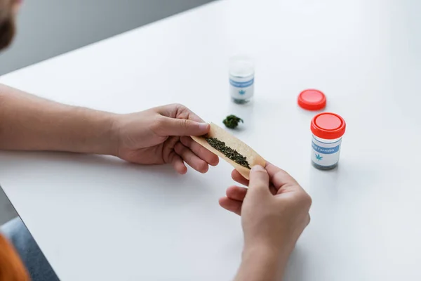 Vista parcial del hombre haciendo articulación con cannabis medicinal seco en casa - foto de stock