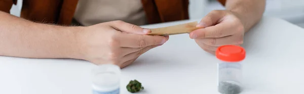 Partial view of ill man making joint with dry medical hemp at home, banner — Stock Photo