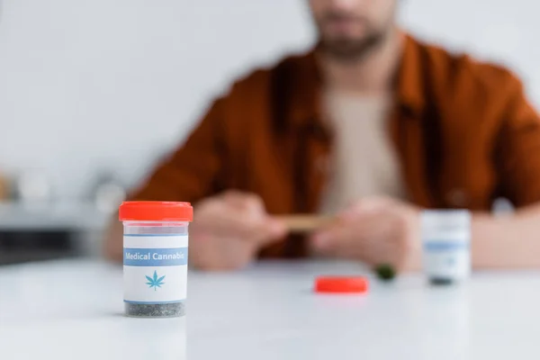 Selective focus of container with dry medical cannabis near blurred man — Stock Photo