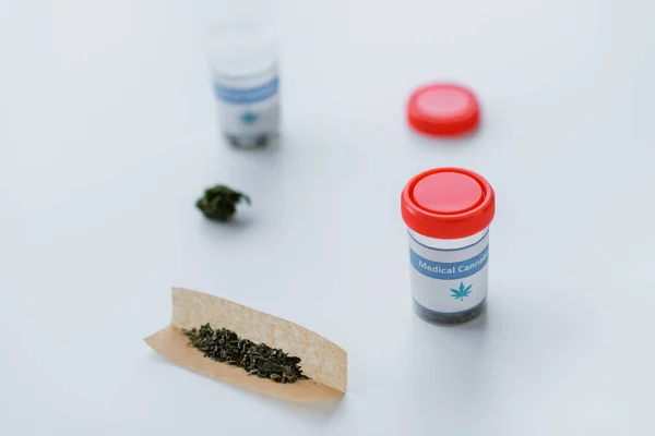 Containers and cigarette paper with dry medical cannabis on white desk — Stock Photo