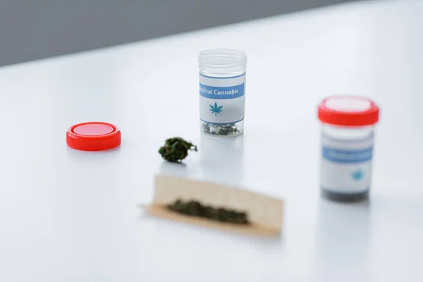 Contenants et papier à cigarettes avec cannabis médical sec sur bureau blanc — Photo de stock