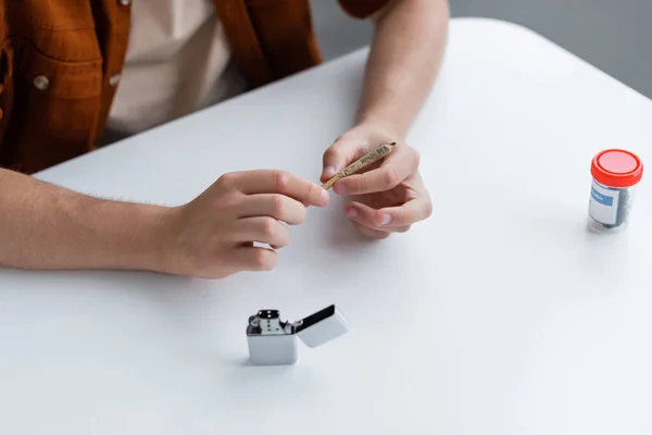 Cropped view of man making joint with medical cannabis near lighter on table — Stock Photo