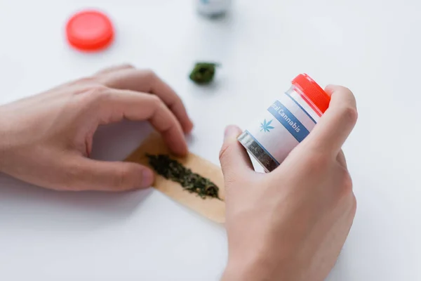 Abgeschnittene Ansicht eines Mannes, der Behälter mit Medikamenten hält, während er Joint mit trockenem medizinischem Cannabis herstellt — Stockfoto