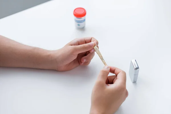 Vista recortada del hombre sosteniendo la articulación de cannabis medicinal cerca de encendedor y tarro — Stock Photo