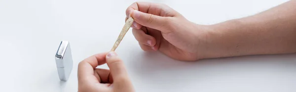 Vista recortada del hombre sosteniendo cigarrillo de cannabis medicinal cerca de encendedor, pancarta - foto de stock