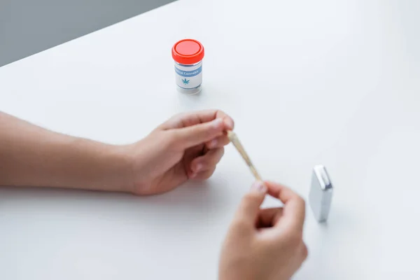 Cropped view of jar with medical cannabis near man holding joint and blurred lighter — Stock Photo