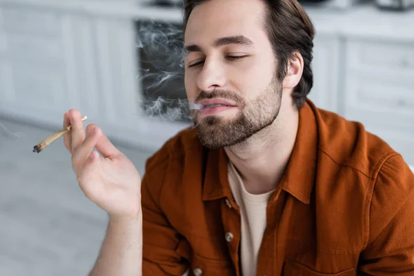 Homem barbudo fumando cigarro de cannabis medicinal em casa — Fotografia de Stock